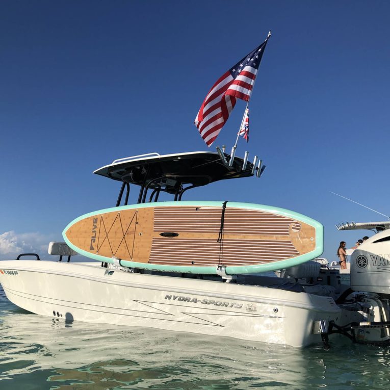 White motorboat transporting a colorful paddleboard on its side with US flag on the top deck.