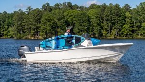 Blue fishing kayak secured in a kayak rack for boat on the side of a white center console cruising on a tree-lined lake